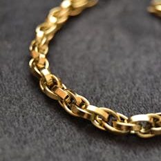 Close-up of a shimmering gold chain necklace on a textured dark surface.
